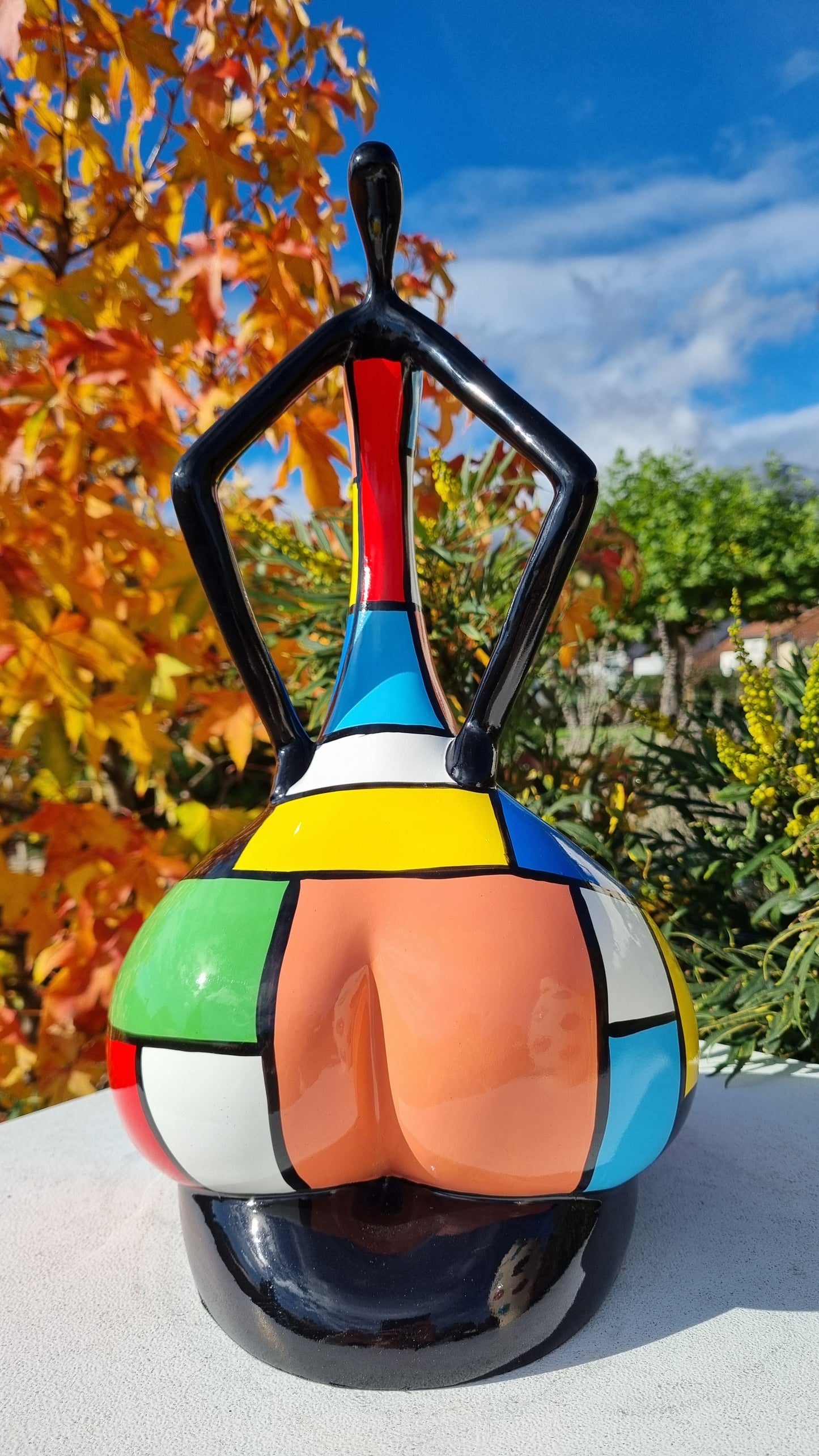 Statue de femme danseuse assise, en résine noire et multicolore, motifs à carreaux. Hauteur 45 centimètres
